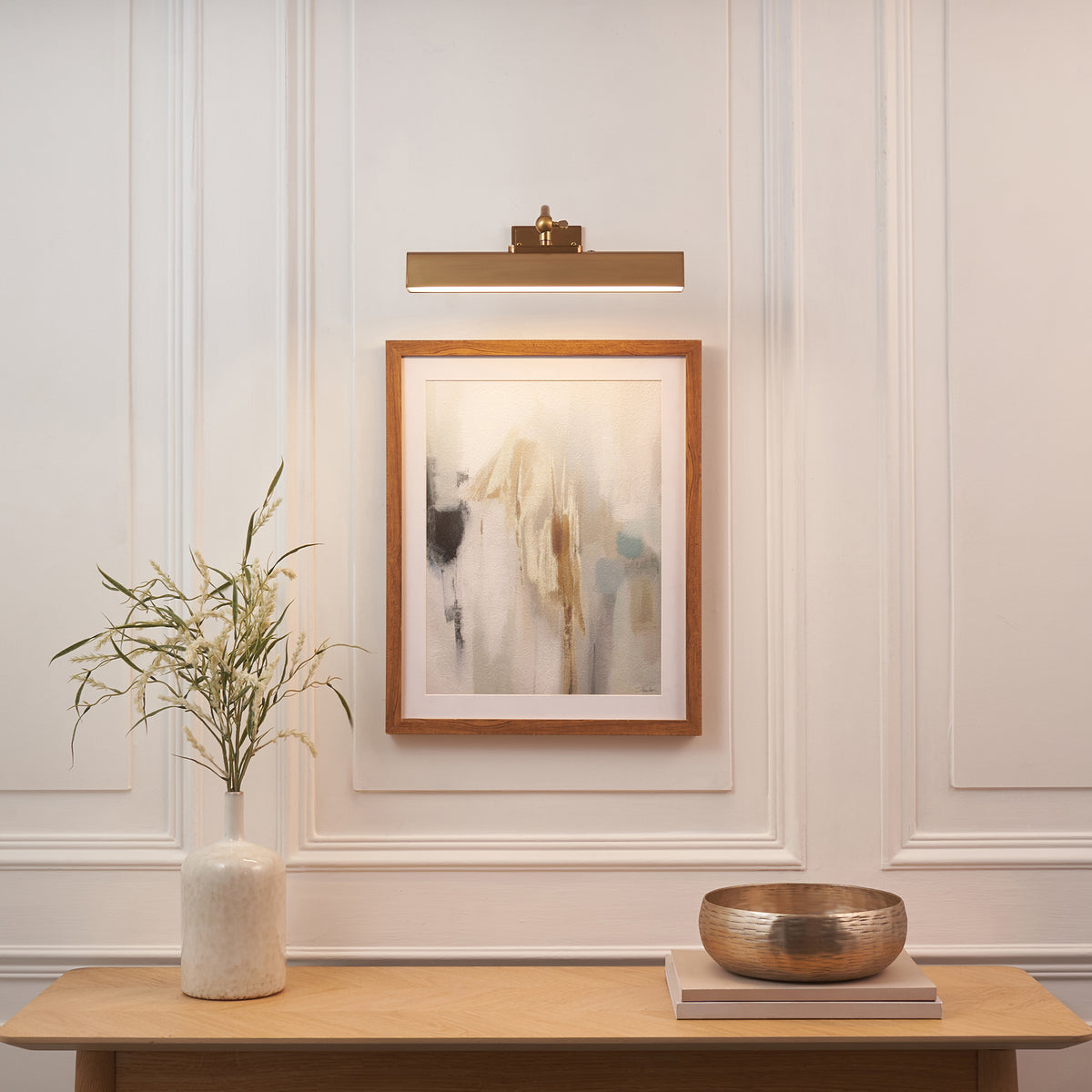 Lasos brass picture light above a framed abstract print on a panelled wall with console styling
