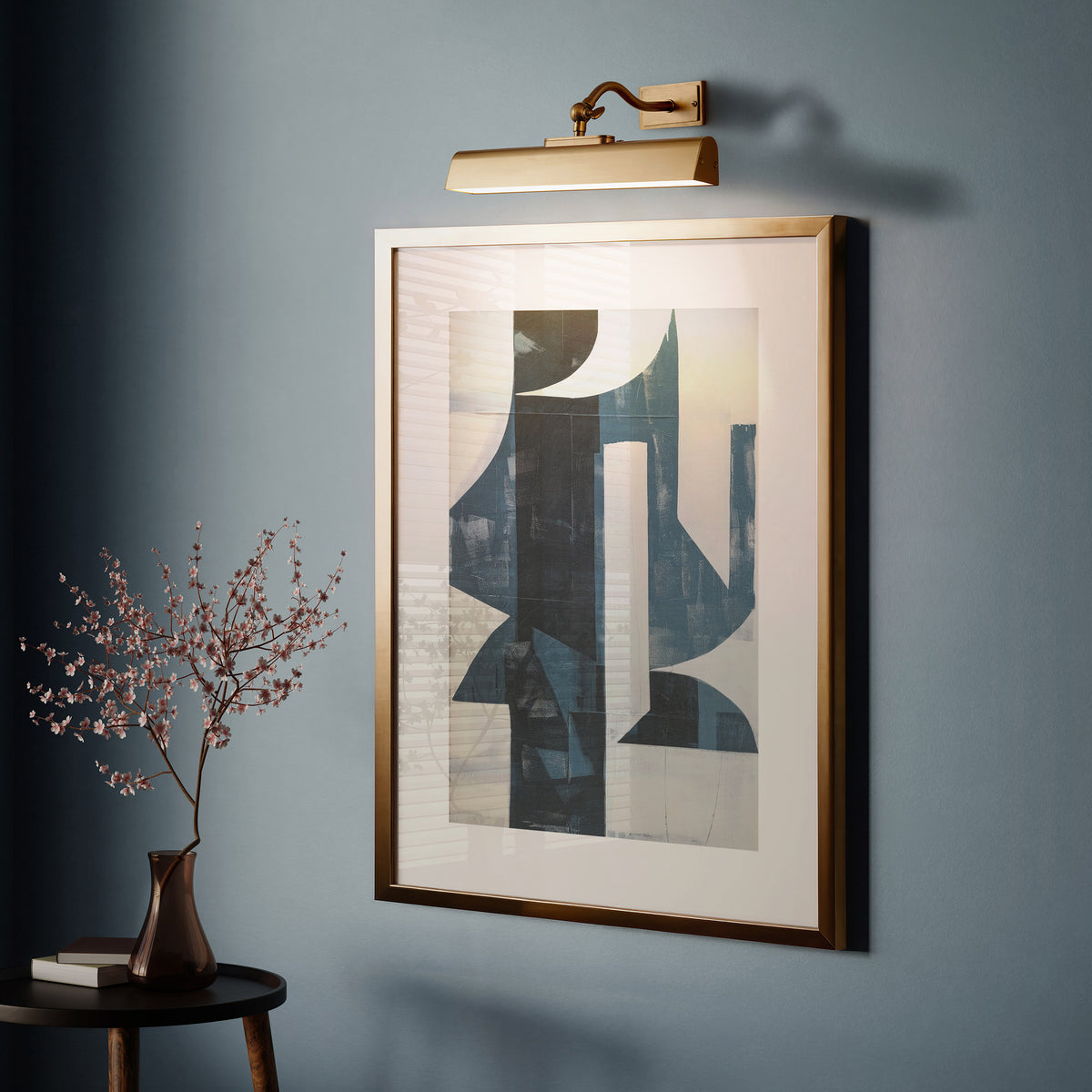 Lasos brass picture light lit above a large framed graphic print on a deep blue wall