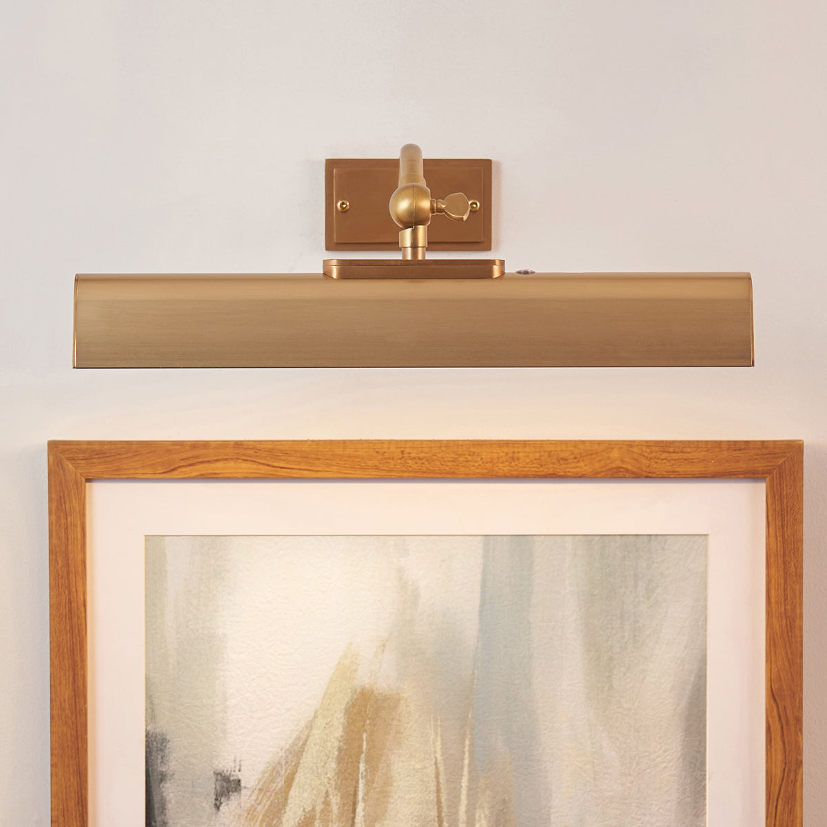 Lasos warm brass picture light glowing above an oak-framed abstract artwork