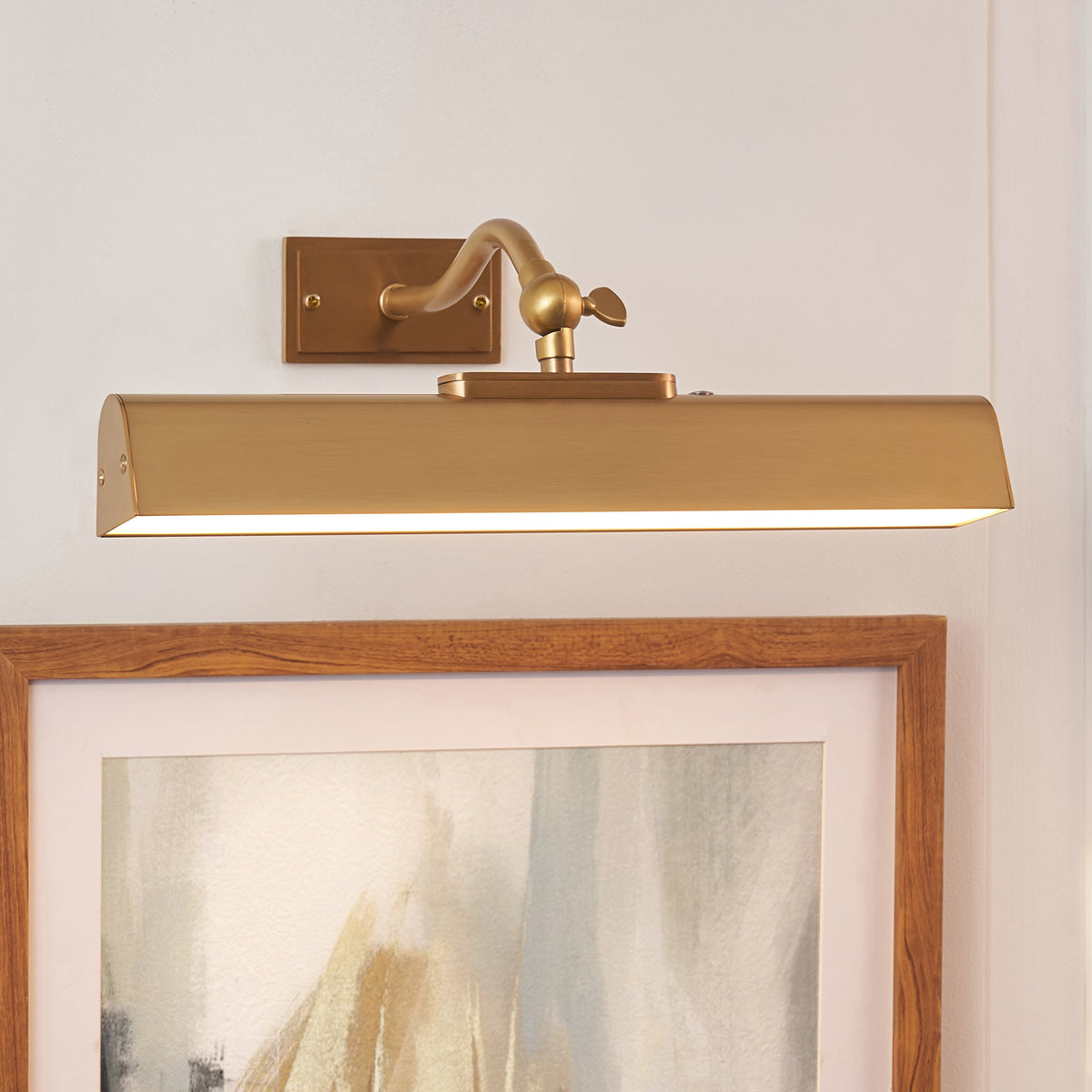 Angled view of the Lasos brass picture light casting warm light down over a timber picture frame