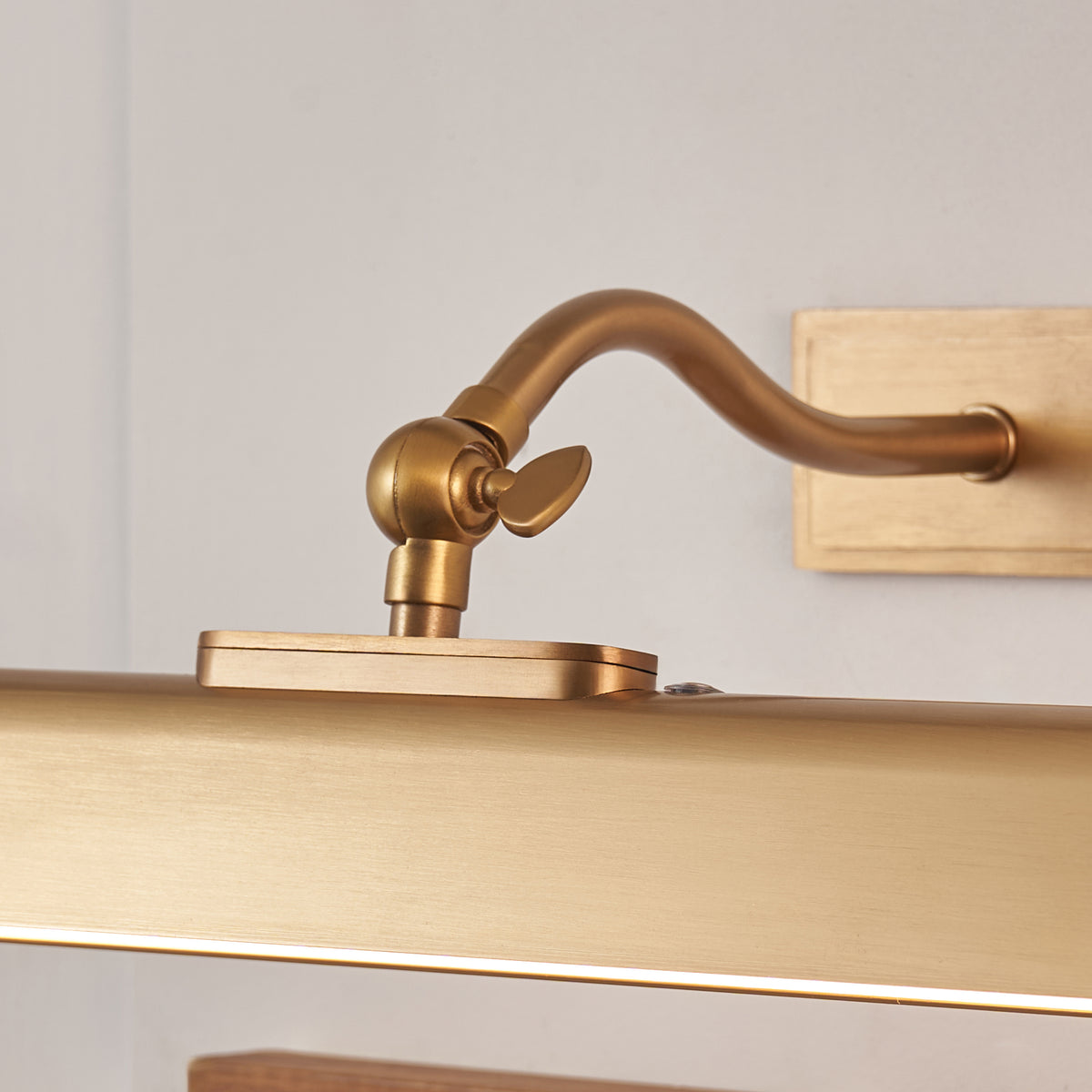 Close-up of the Lasos picture light's curved brass arm, tilt knuckle and square backplate