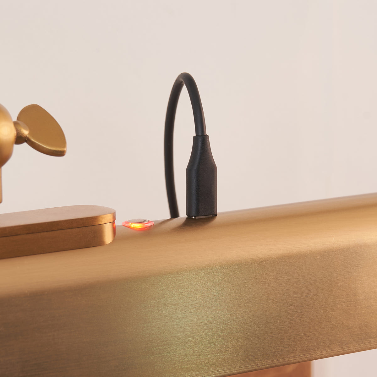 Detail of the Lasos light's magnetic charging cable and red charging indicator on brass shade