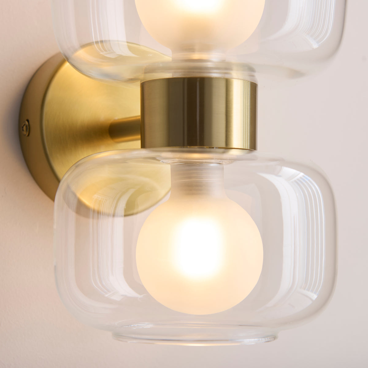 Close-up of the Rossano wall light's polished brass stem and clear glass shades