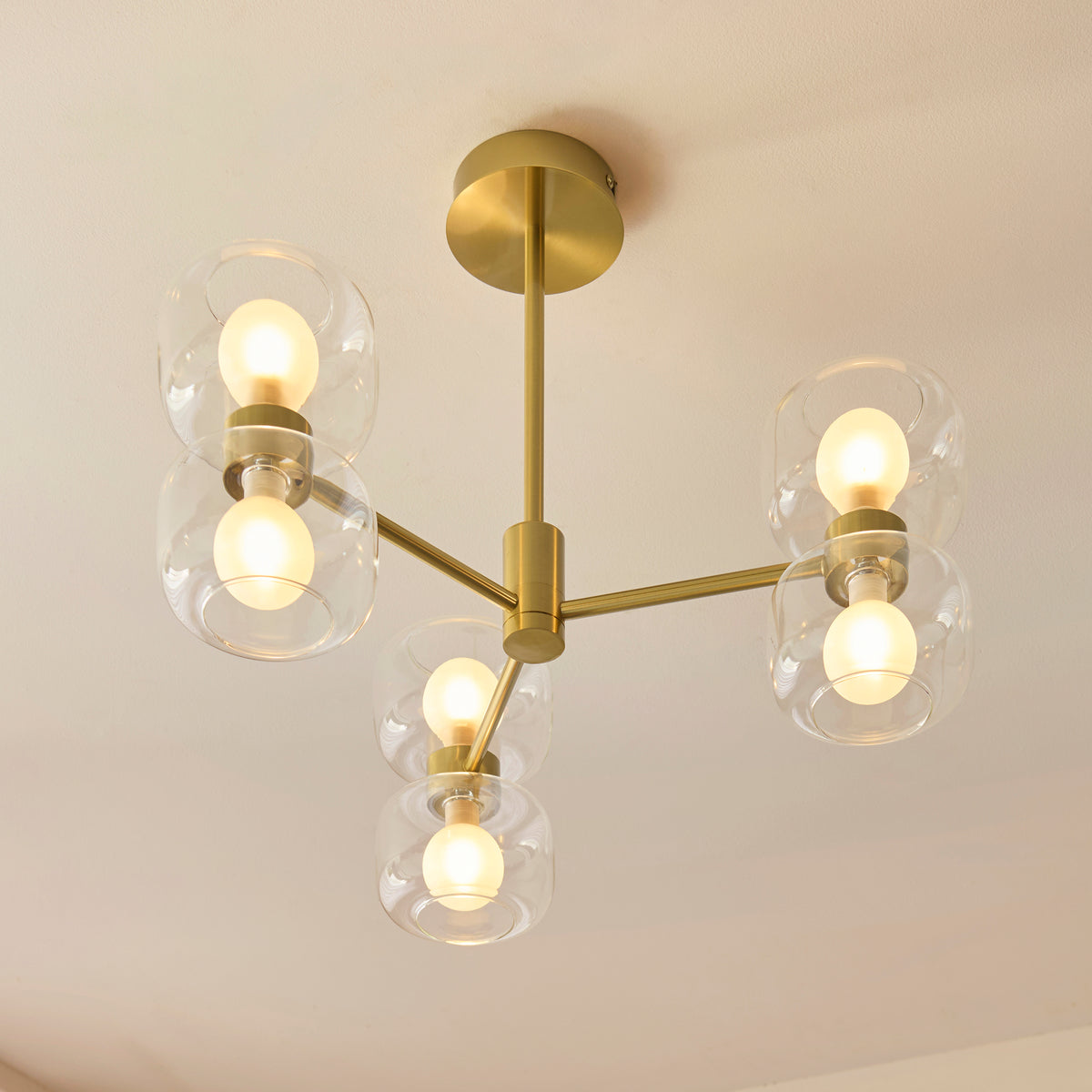 Rossano brass ceiling light viewed from below, its six frosted globes lit within clear glass