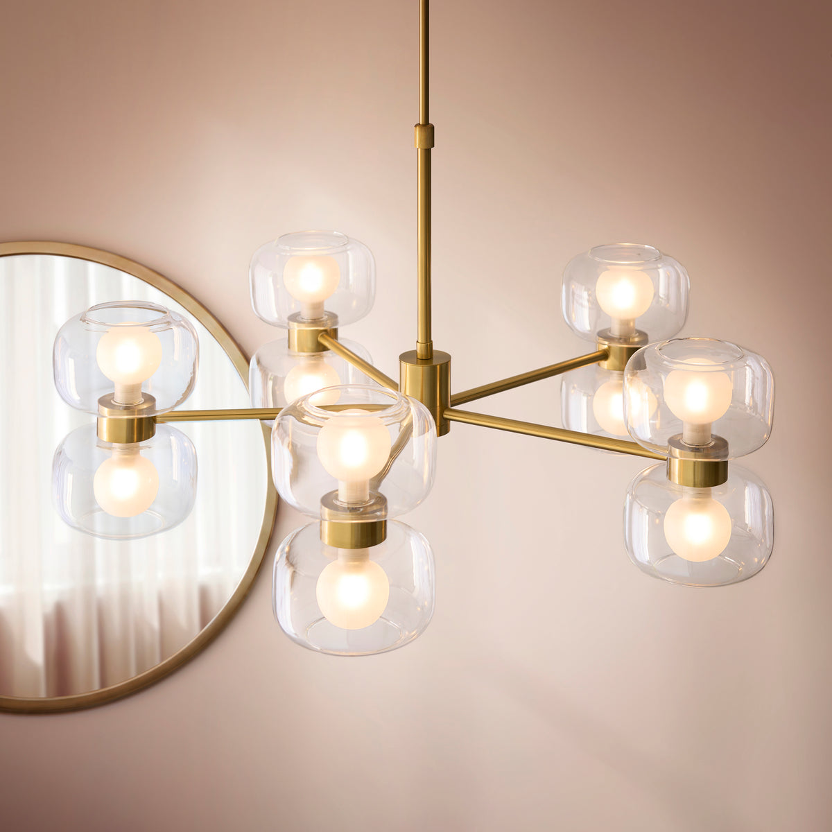 Rossano brass chandelier with clear glass shades seen beside a round wall mirror