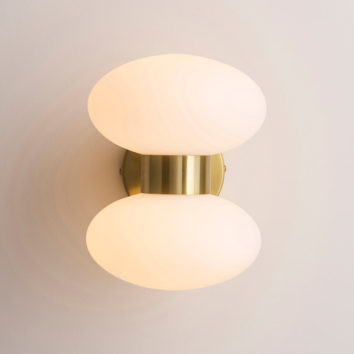 Front-on view of the Rossano wall light showing two opal glass ovals and a brushed brass band