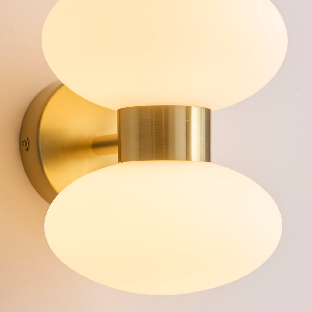 Close-up of the Rossano wall light's brushed brass backplate and collar between opal shades