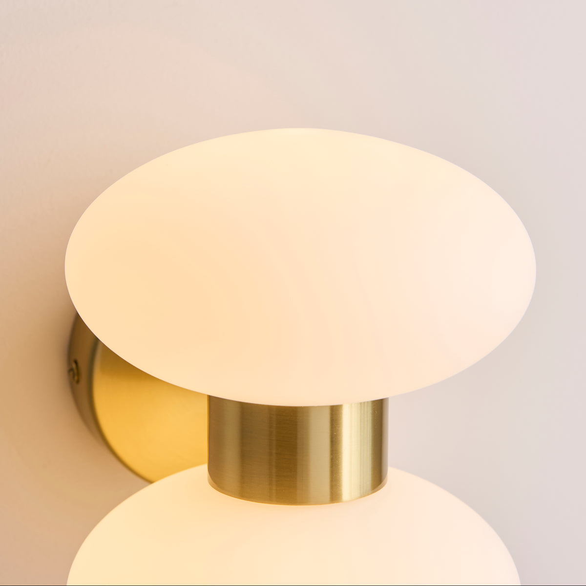 Detail of the upper opal glass oval shade and warm brass cylinder on the Rossano wall light