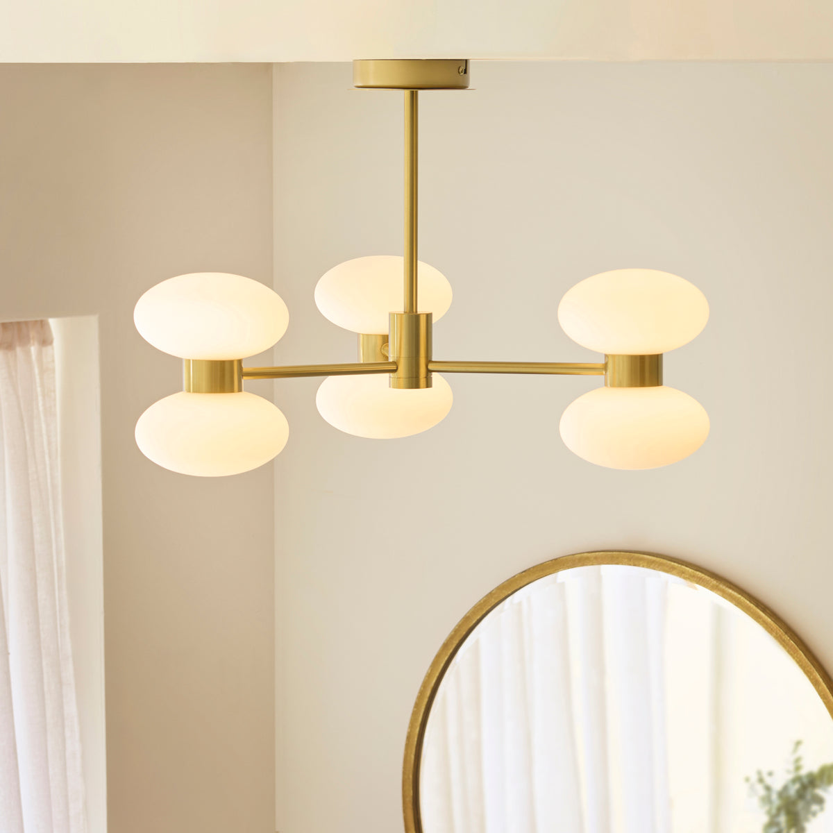 Rossano brass semi flush ceiling light lit above a round brass mirror in a neutral room