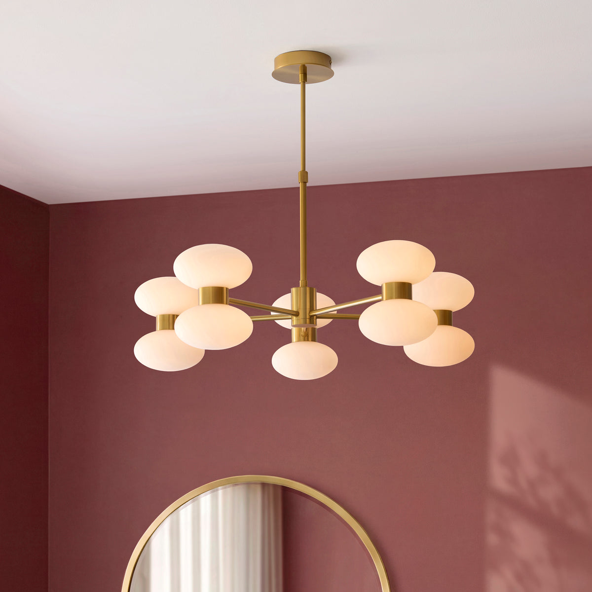 Rossano brass pendant lit above a round mirror in a deep burgundy dining room