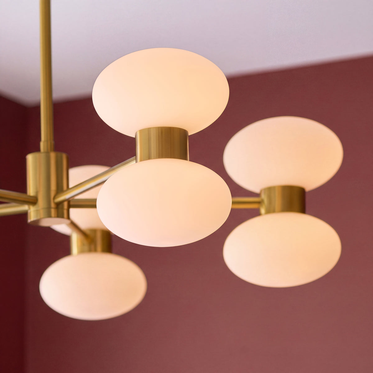Close-up of the Rossano pendant's opal glass ovals against a burgundy wall