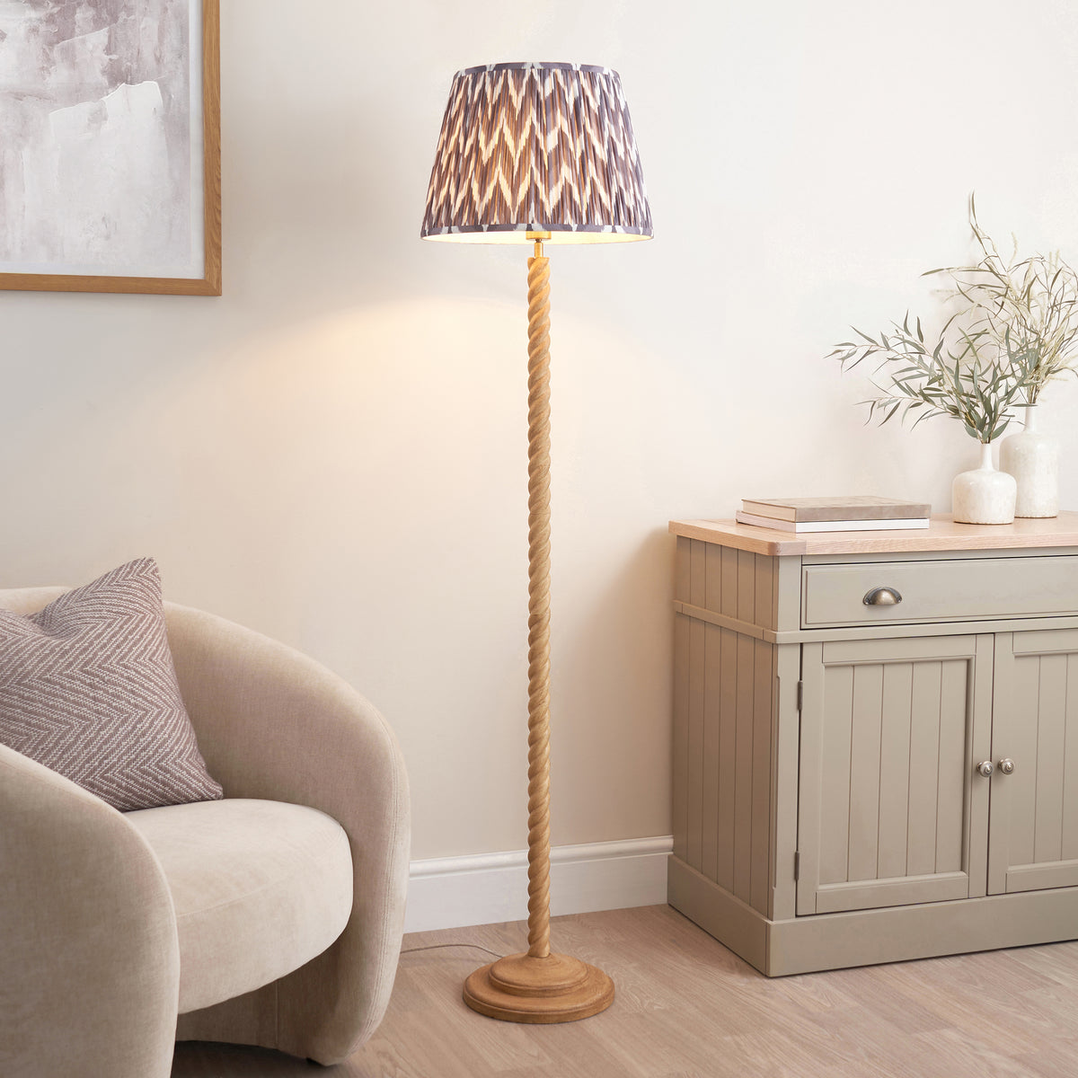 Twist & ZigZag oak effect floor lamp lit in a living room beside a boucle chair and sideboard