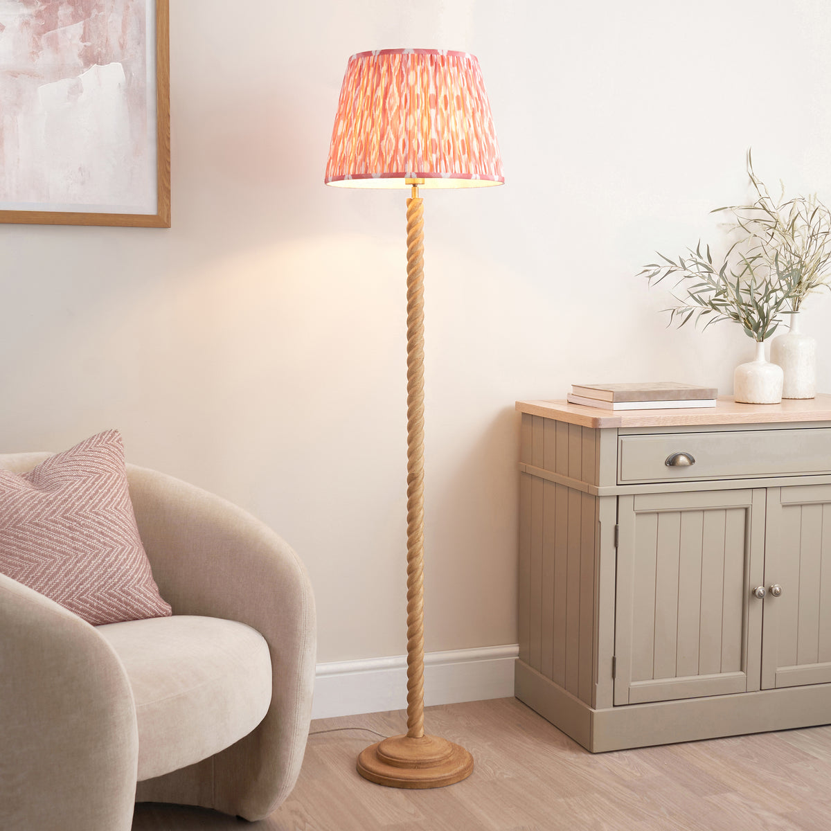 Coral pink ikat floor lamp lit in a living room with boucle armchair and grey sideboard