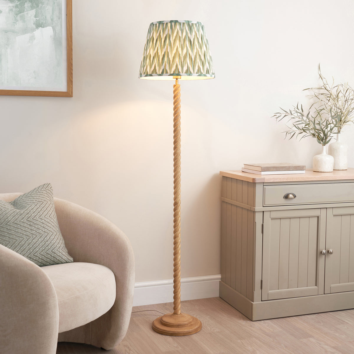 Green zigzag floor lamp lit in a living room with boucle chair, sideboard and olive branches