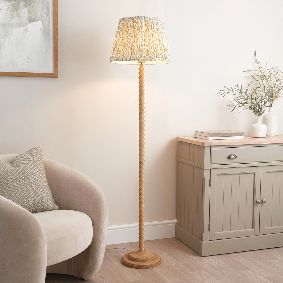 Green leaf print floor lamp lit beside a boucle armchair and grey sideboard in a living room