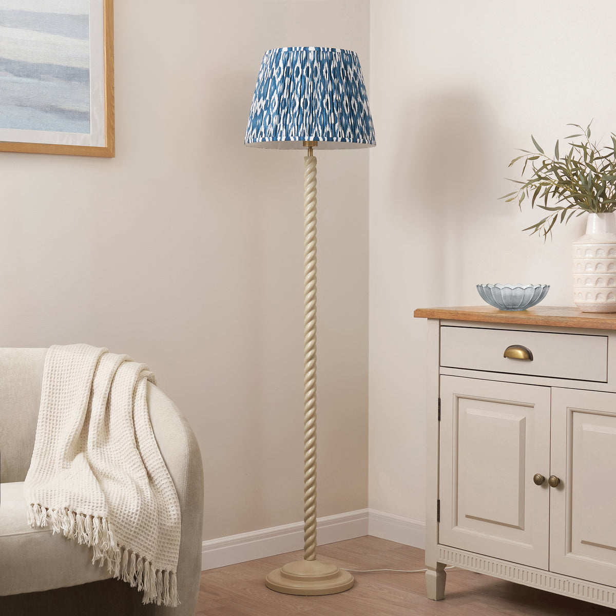 Almond white twisted floor lamp with blue ikat shade in a neutral living room next to an oak-topped sideboard
