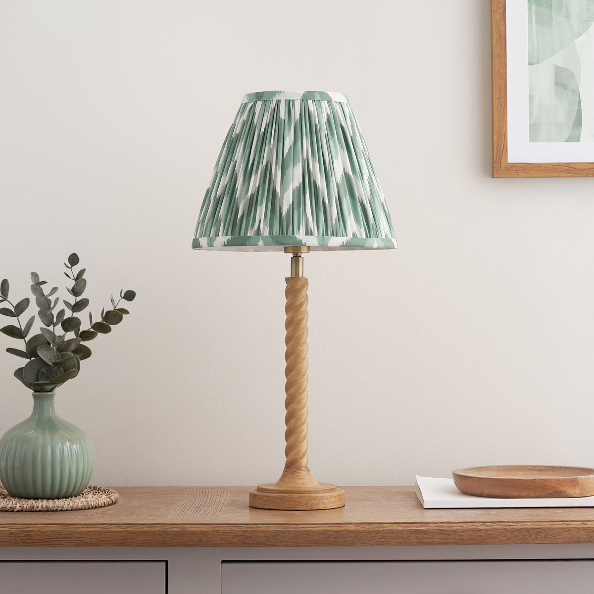 Oak effect twisted table lamp with green zigzag ikat shade styled on a wooden console with a bowl