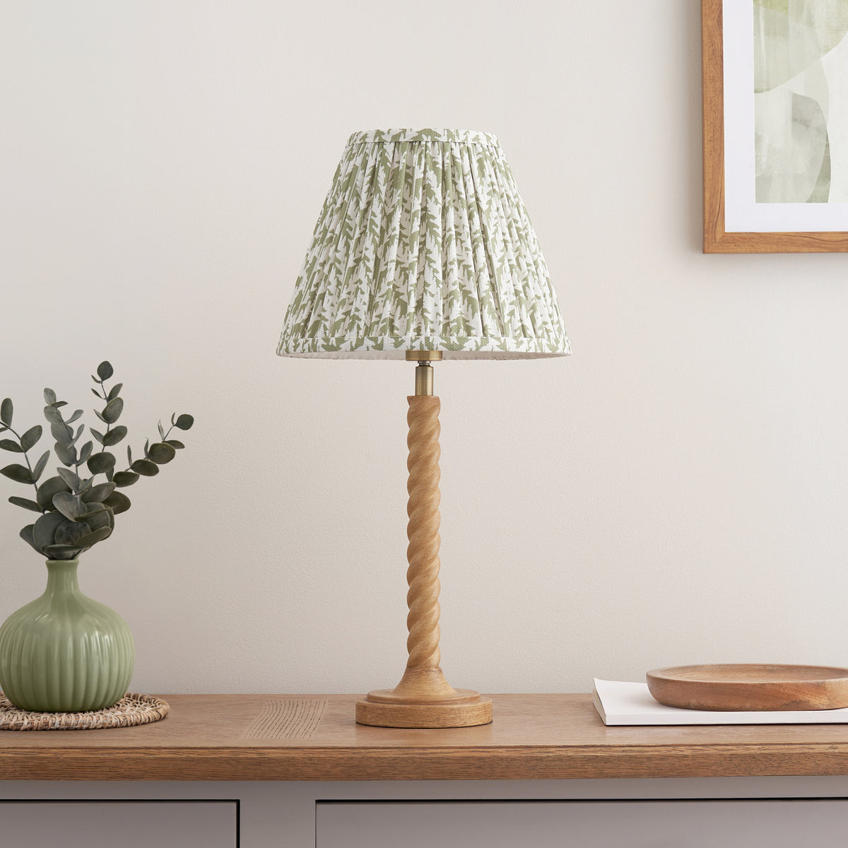Oak effect twisted table lamp with green leaf patterned shade on a wooden console below framed art