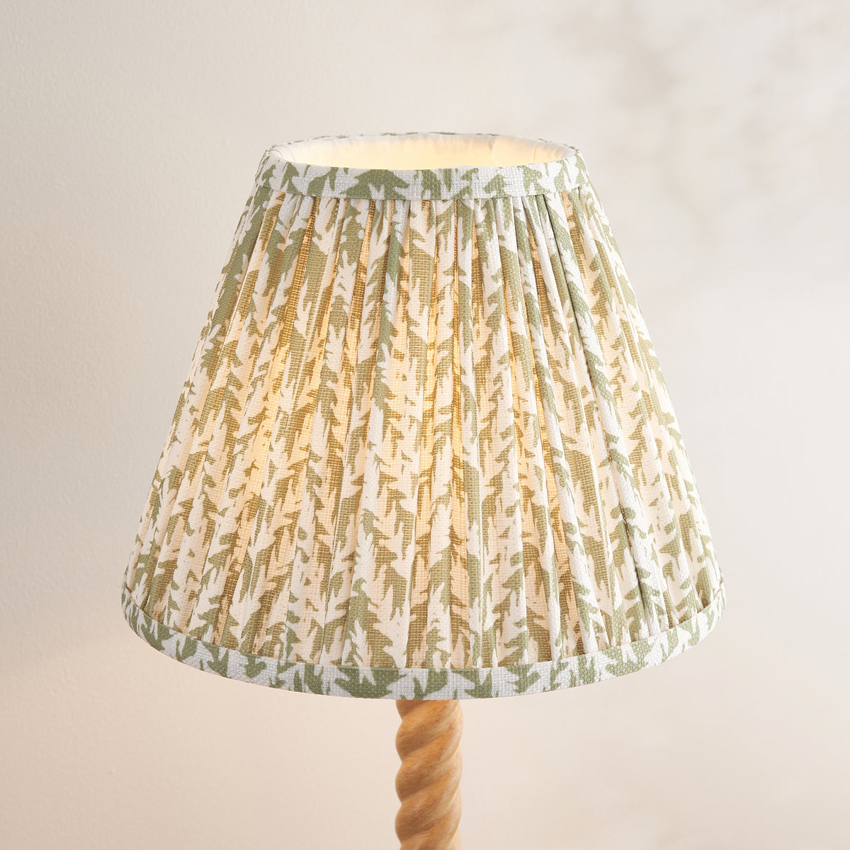 Close-up of the pleated cream shade with green leaf motifs above the twisted stem