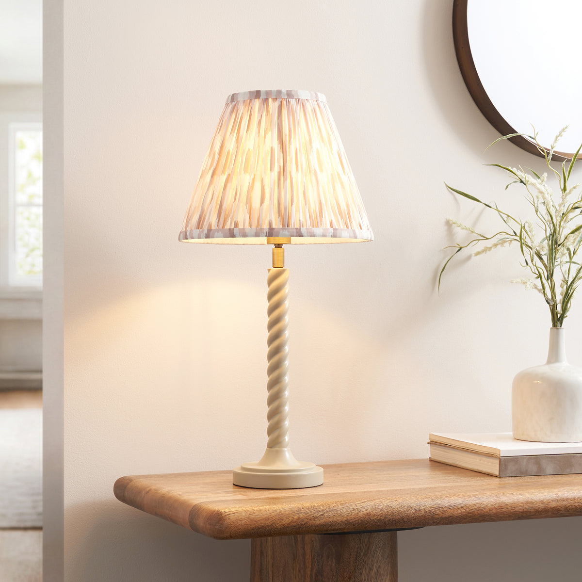 Twist & Ikat table lamp lit on an oak console table beside a round mirror and stoneware vase