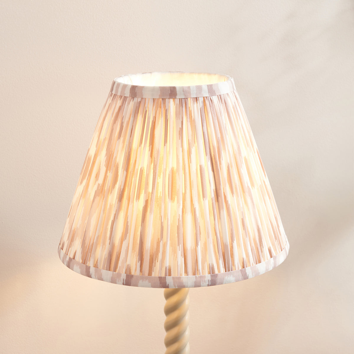 Close-up of the pleated neutral ikat fabric shade glowing on the Twist & Ikat table lamp