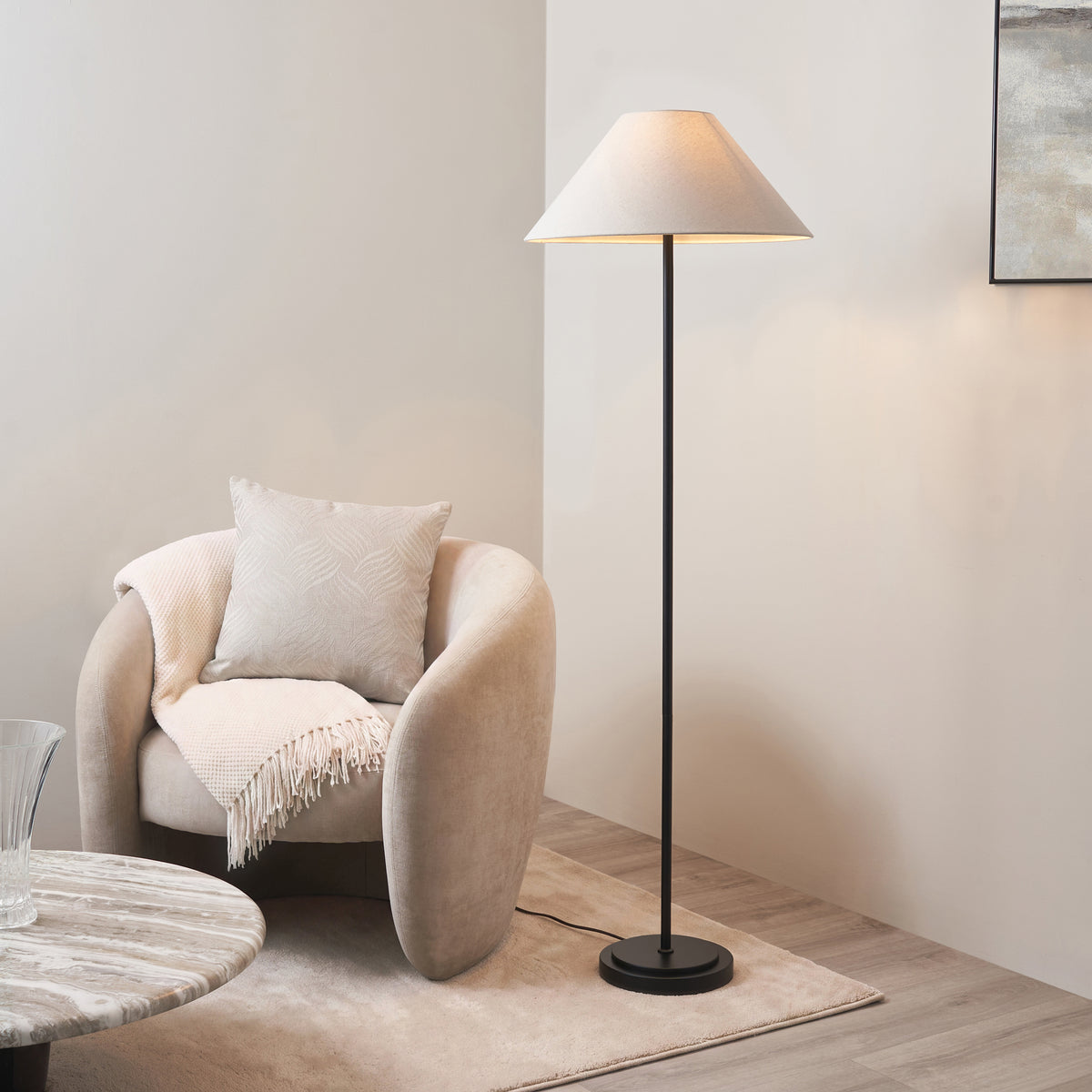 Arlo floor lamp lit beside a cream boucle armchair, marble coffee table and neutral rug