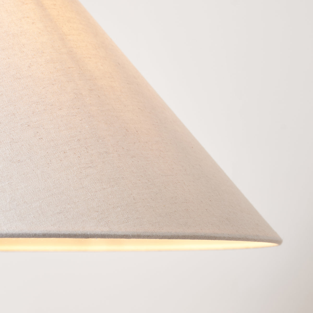 Underside of the lit natural linen coolie shade showing its warm glow and textured weave