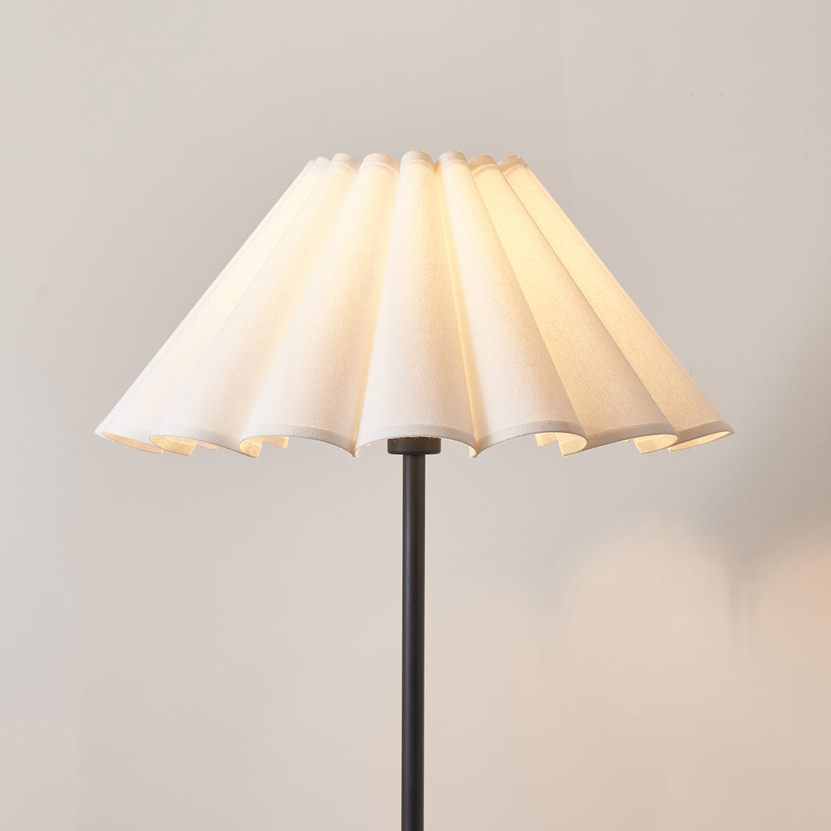 Close-up of the white scalloped pleated shade glowing on the matt black Arlo stem