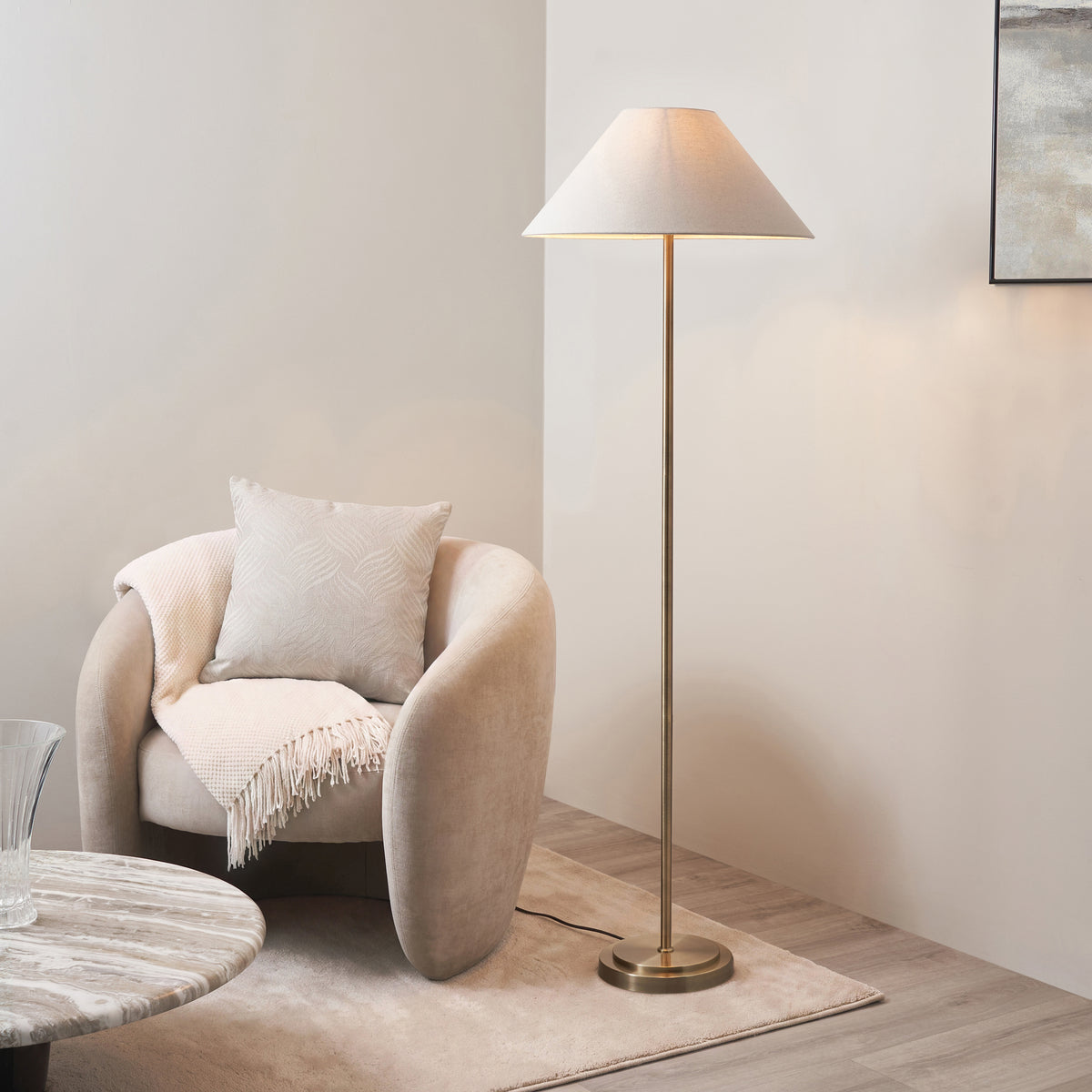 Antique brass Arlo floor lamp lit beside a cream boucle armchair and marble coffee table