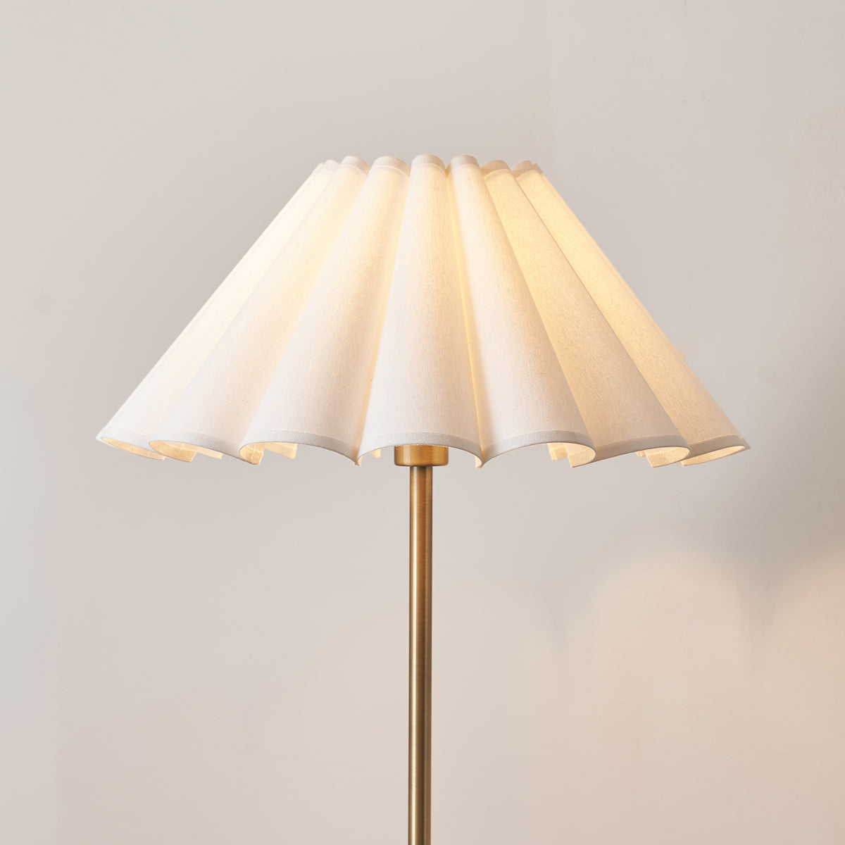 Close-up of the ivory scalloped pleated shade glowing above the antique brass stem