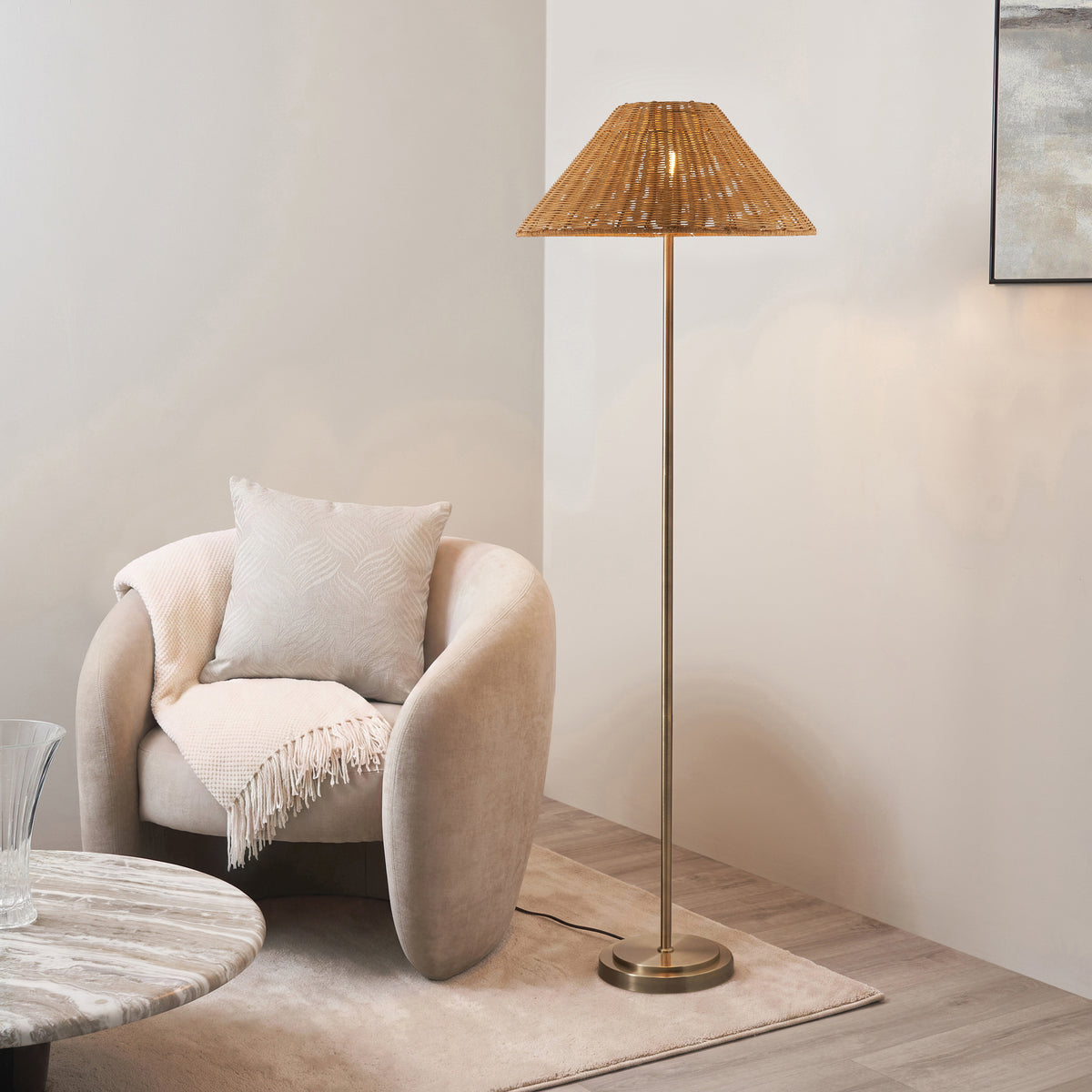 Brass Arlo floor lamp with brown rattan shade lit beside a cream boucle armchair