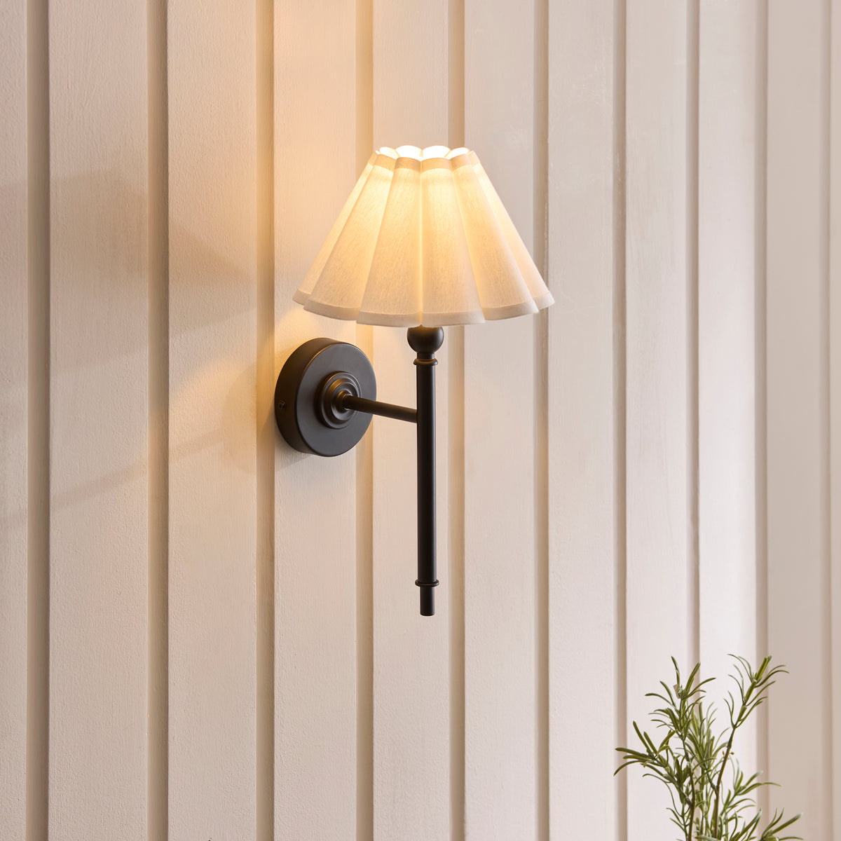 Sylvie wall light lit on panelled walls, its scalloped white shade casting a soft warm glow