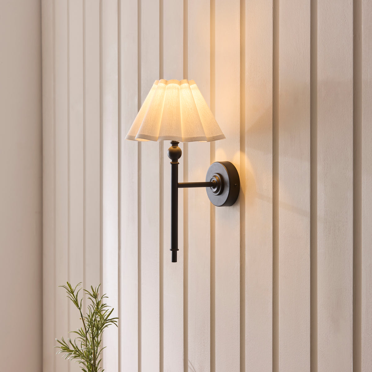Angled view of the Sylvie matt black wall light and pleated white shade mounted on panelling