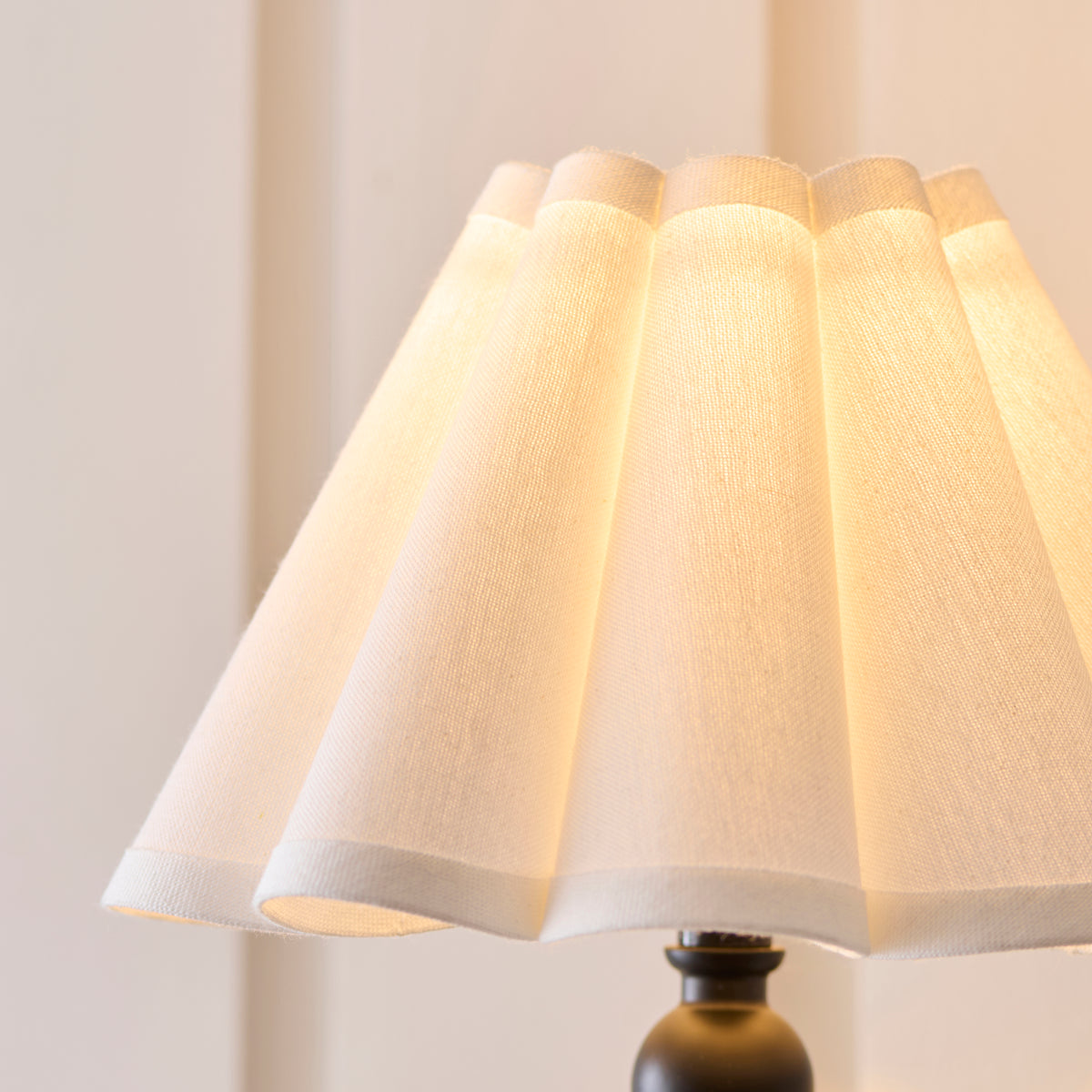 Detail of the softly lit pleated white fabric shade on the Sylvie wall light