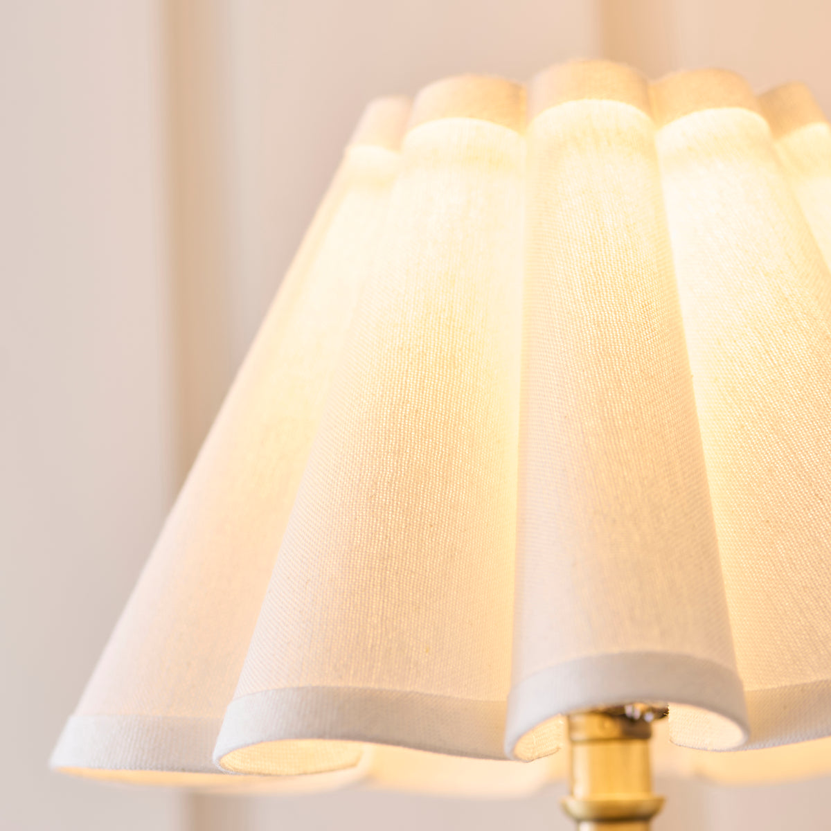 Detail of the warmly lit pleated shade above the antique brass fitting of the Sylvie light