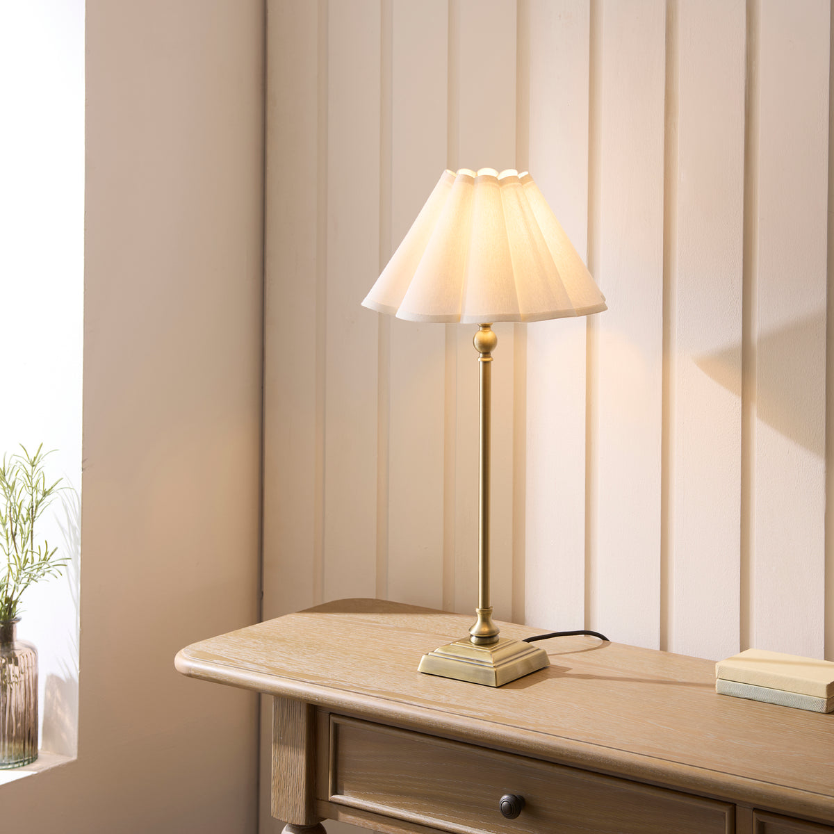 Sylvie antique brass table lamp glowing on a console table beside a window