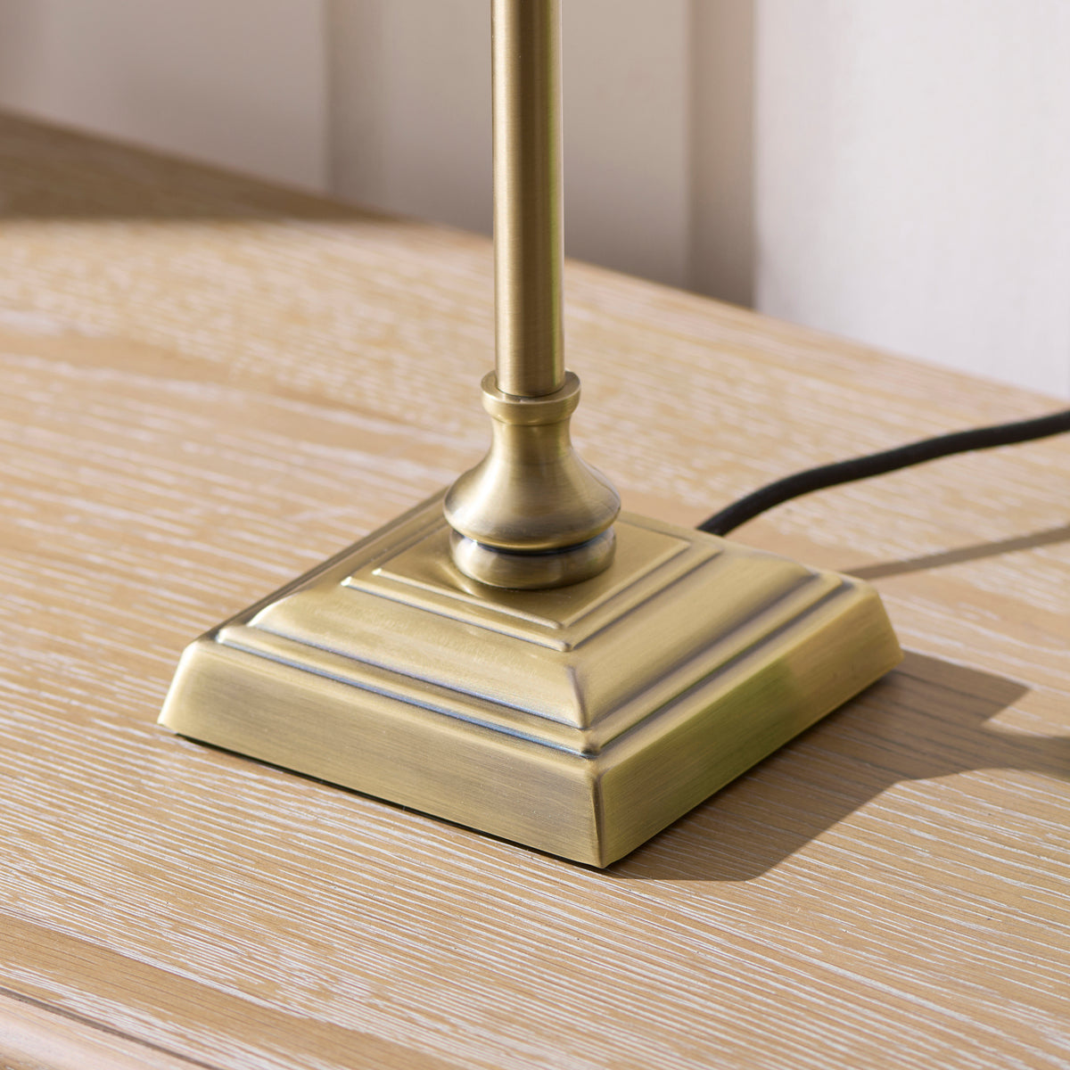 Stepped square antique brass base of the Sylvie table lamp on pale wood