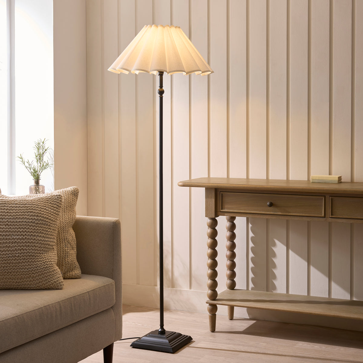 Sylvie matt black floor lamp lit beside a sofa and wooden console in a neutral living room