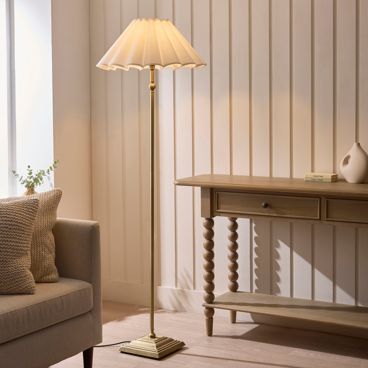 Sylvie antique brass floor lamp lit beside a sofa and wooden console table in a bright living room