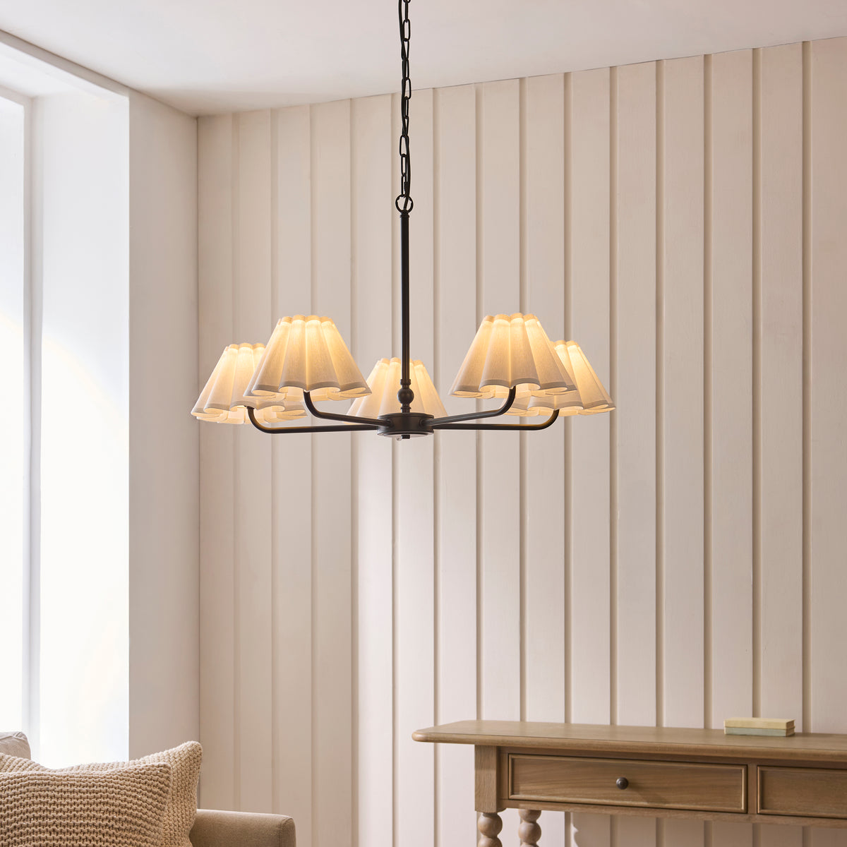 Sylvie matt black five-light pendant hanging lit above a console table in a panelled room