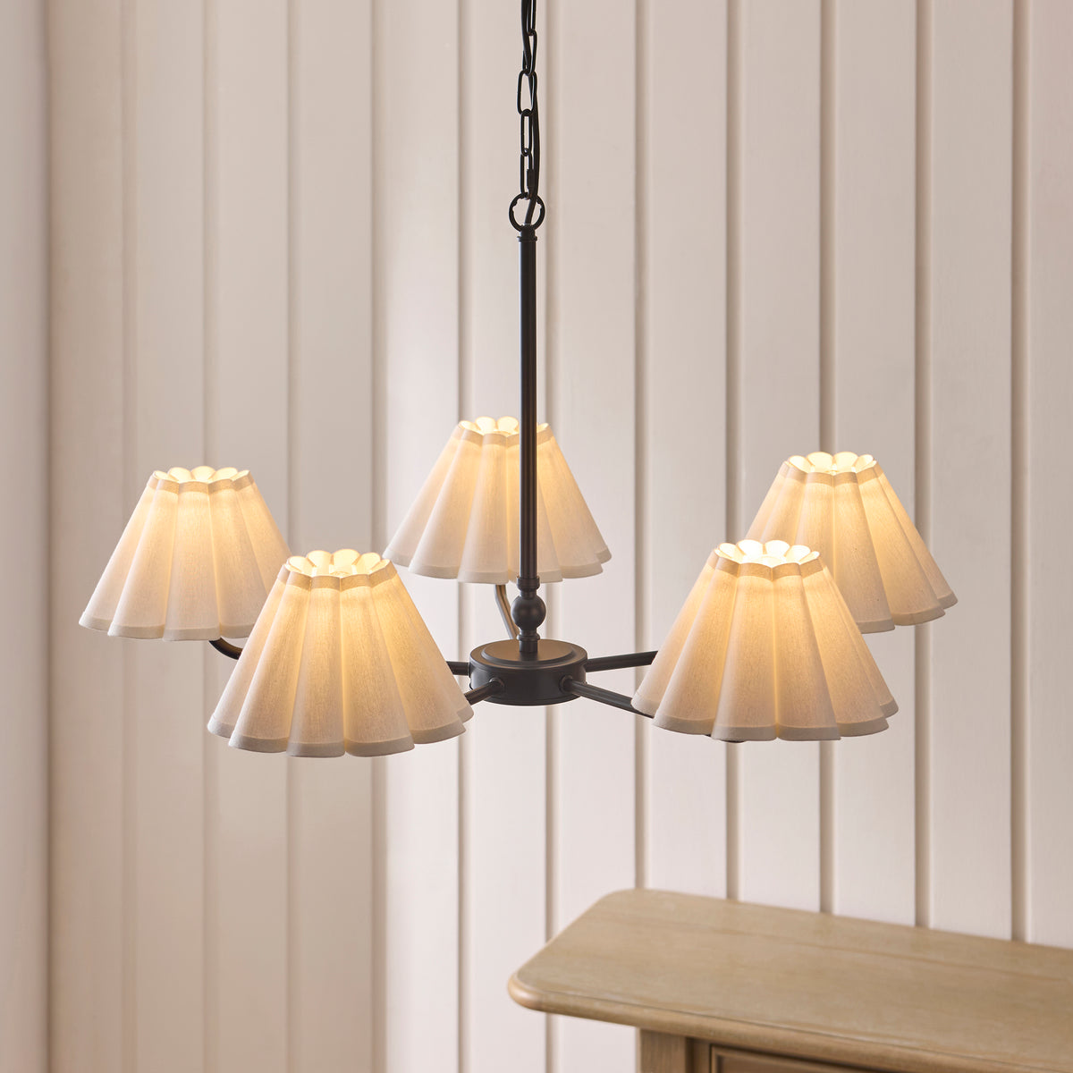 Sylvie black chandelier with five glowing scalloped shades against cream panelled walls