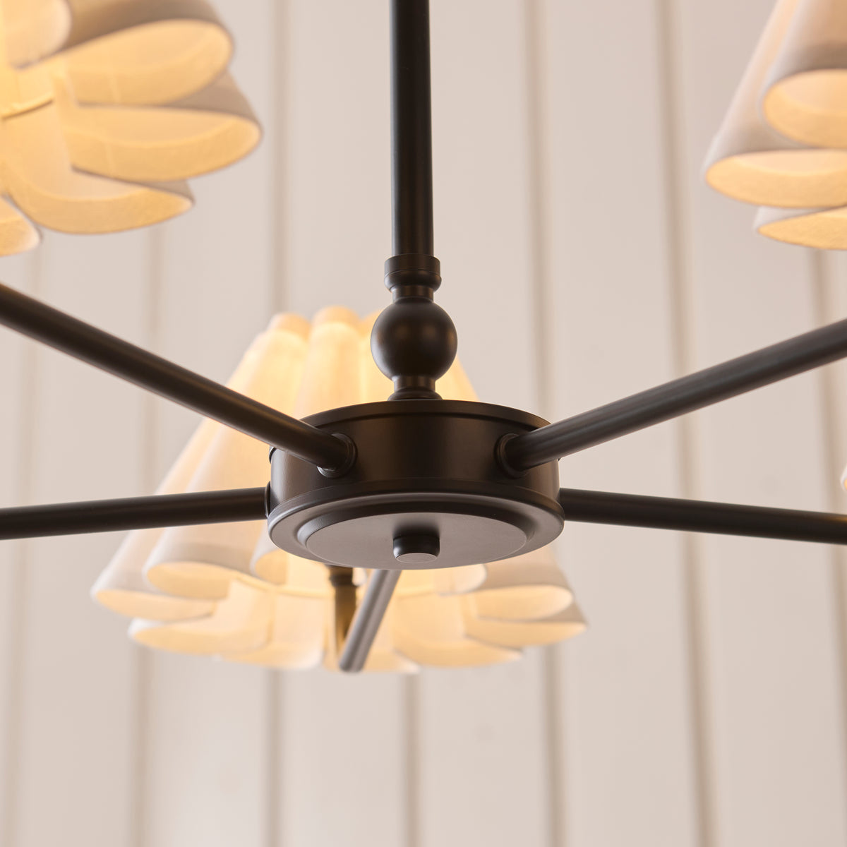 Underside view of the Sylvie pendant's black hub with radiating arms and lit shades