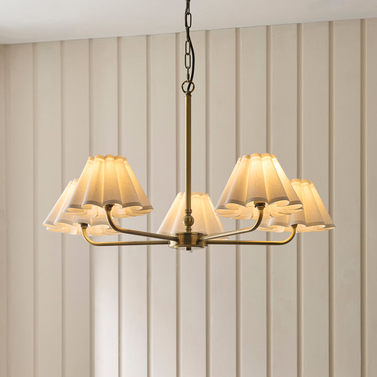 Sylvie brass five-arm pendant with cream pleated scalloped shades against a cream panelled wall