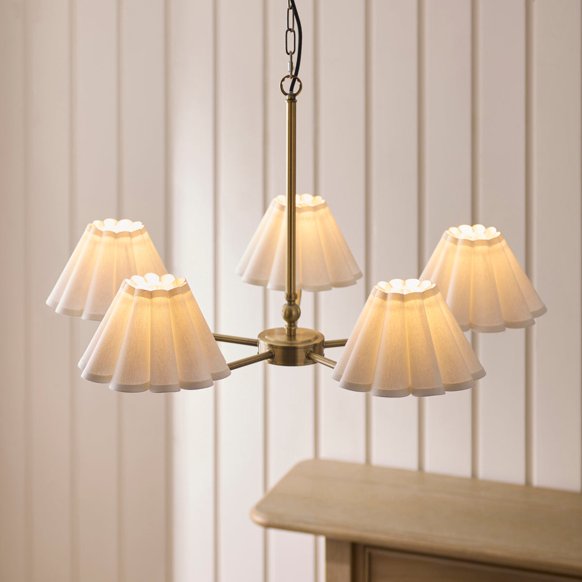 Sylvie antique brass pendant lit from below, showing five glowing scalloped fabric shades