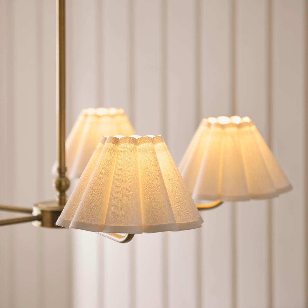 Close-up of the Sylvie pendant's pleated scalloped shades glowing warmly on brass arms
