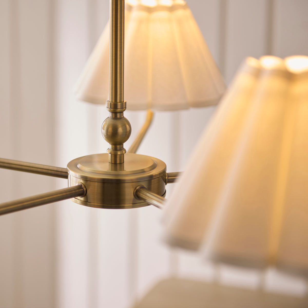 Detail of the Sylvie pendant's antique brass central hub and ball finial beneath lit shades