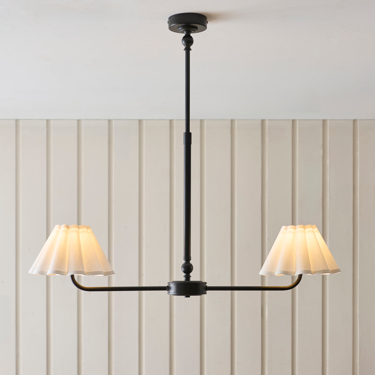 Sylvie black linear pendant with two glowing white scalloped shades against a panelled wall