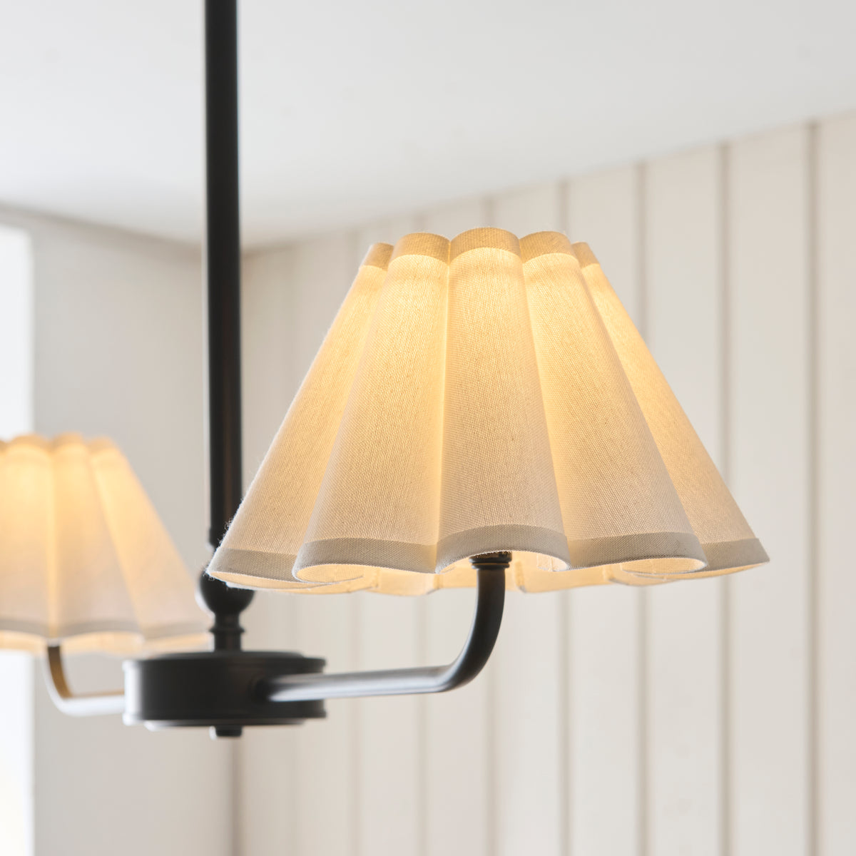 Close-up of the Sylvie pendant's white pleated scalloped shade glowing on a black arm