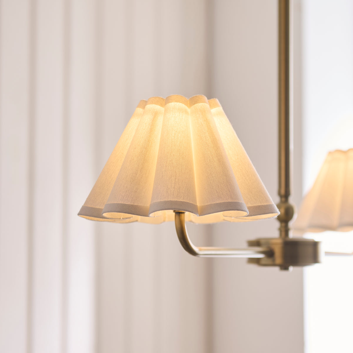 Close-up of the Sylvie pendant's cream pleated scalloped shade lit on a brass arm