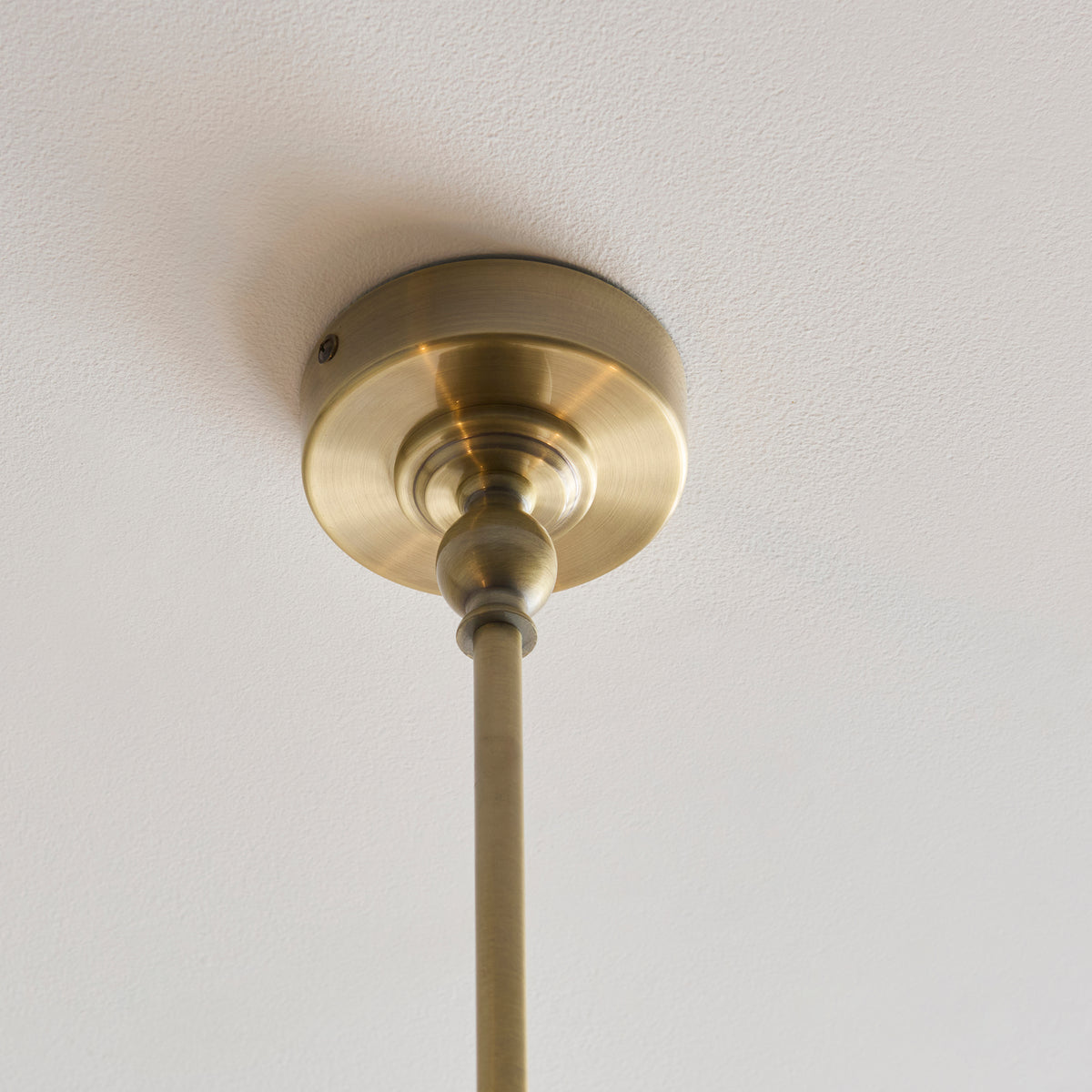 Antique brass ceiling rose and stem of the Sylvie linear pendant on a white ceiling